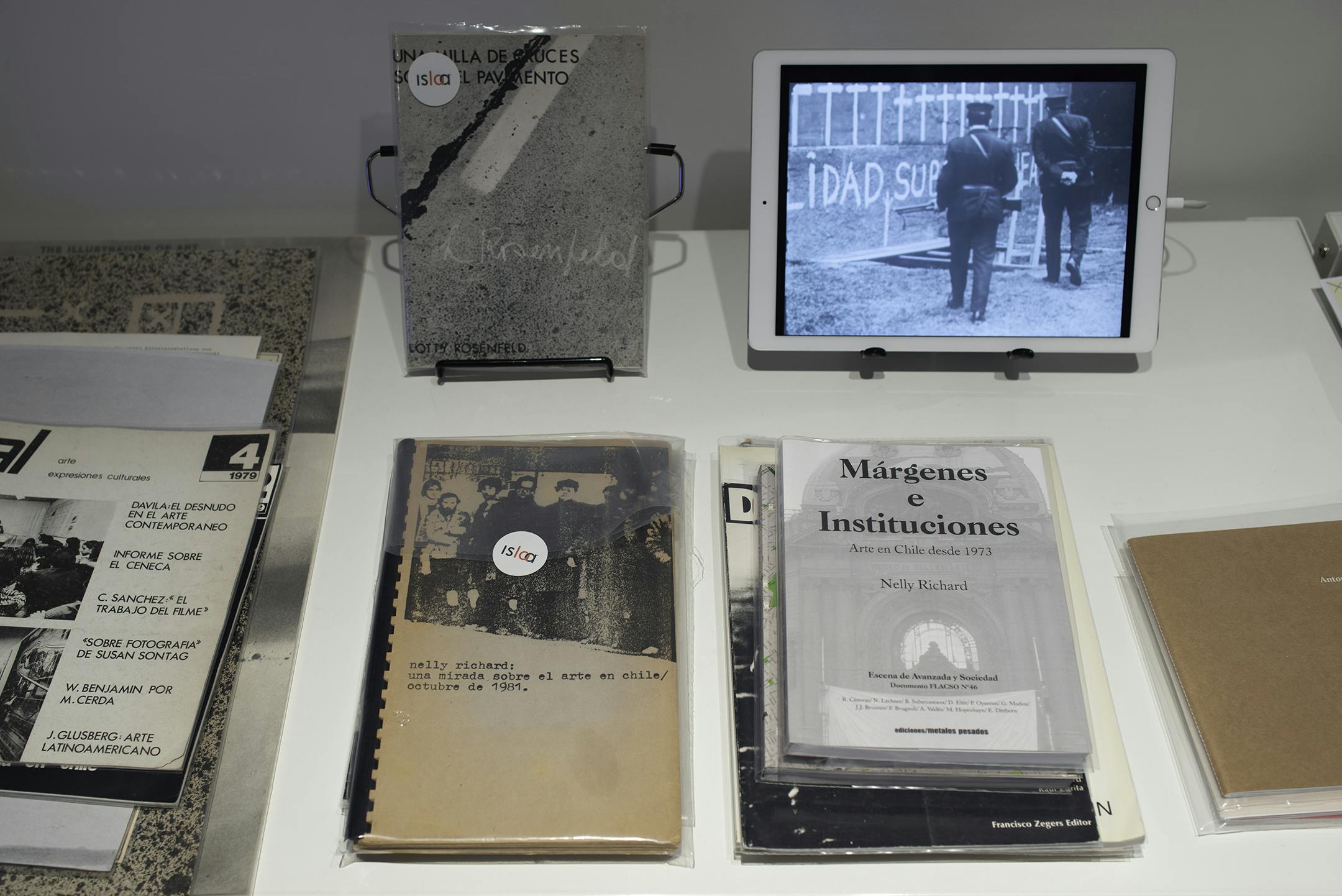 Stacks of original documents and booklets next to a smart tablet playing video.