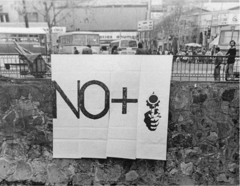 Black and white photograph of a white poster with the text "NO +" and a hand holding a gun painted on its surface.