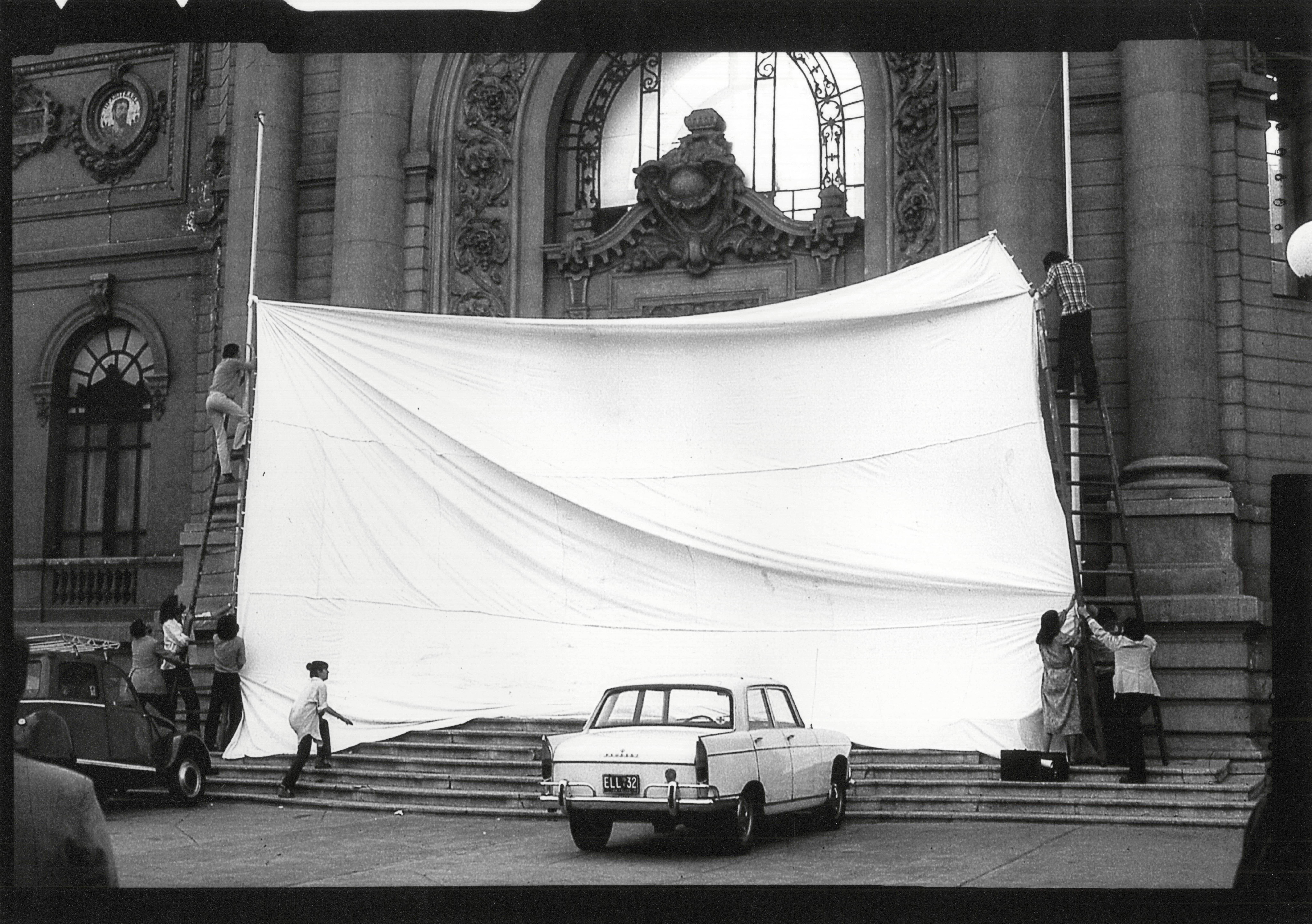Black and white photograph of a group of people installing a large white sheet in front of the entrance to the Museo de Bellas Artes.