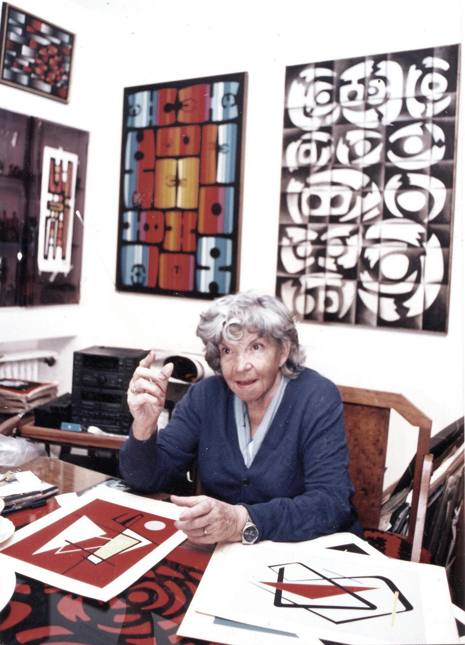 María Freire sitting at a desk surrounded by her paintings.