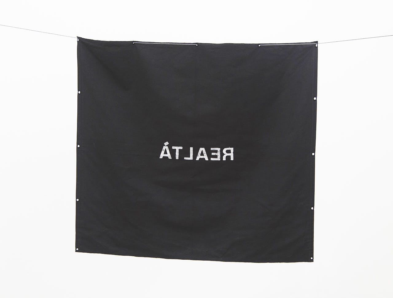 Black and white image of a black fabric square with "REALTÀ" written backwards in white on the surface.
