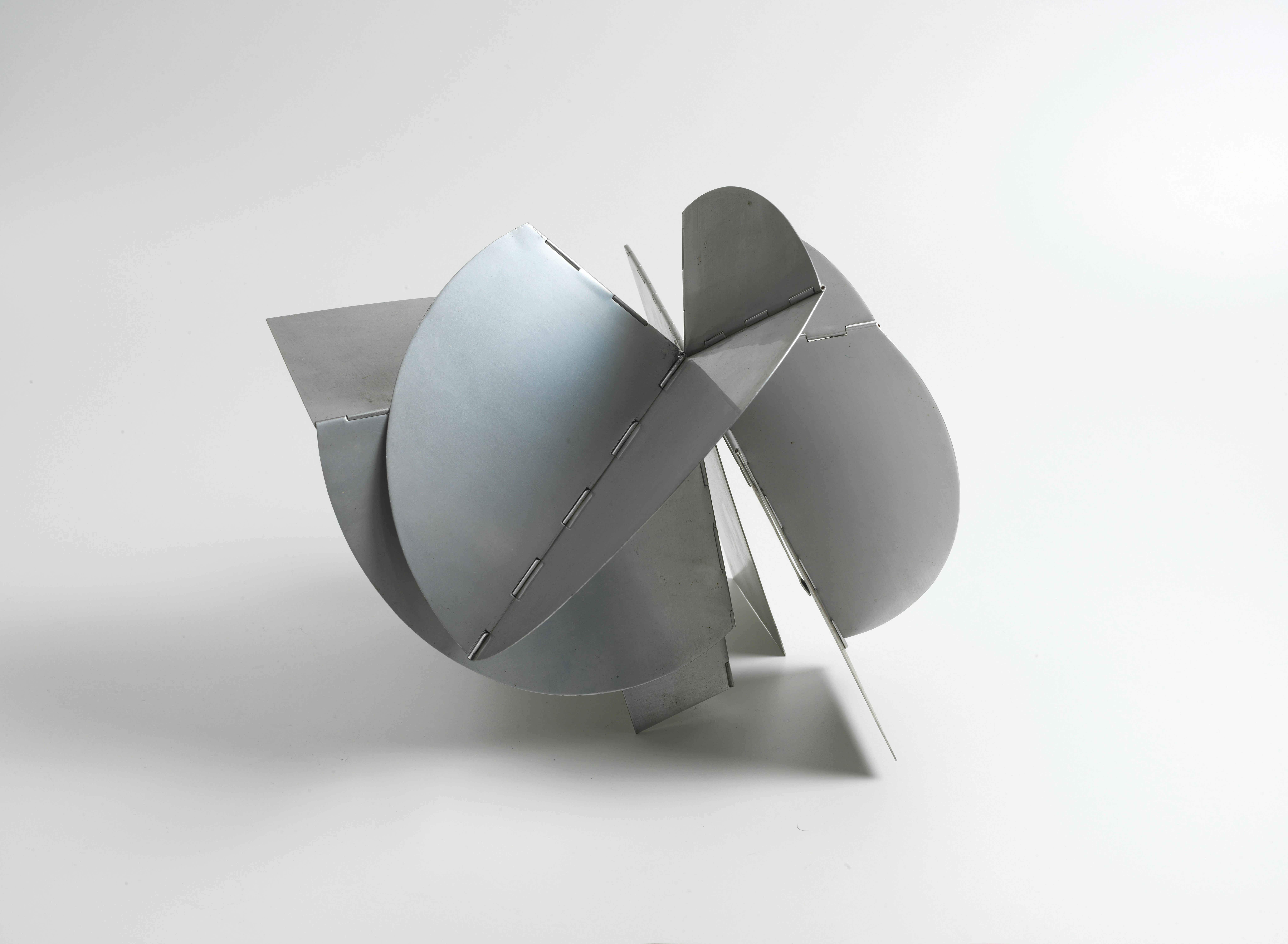 A small sculpture made with thin pieces of silver sheet metal is arrayed at various angles. The various planes of the work range in shape from rectangles to semicircles and are fitted together at acute angles. Several of the vertices between them are hinged, so that the various places of the work can be adjusted by hand.