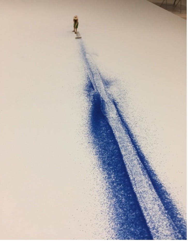 Miniature plastic figurine of a woman wearing a hat and sweeping the white floor with blue paint powder