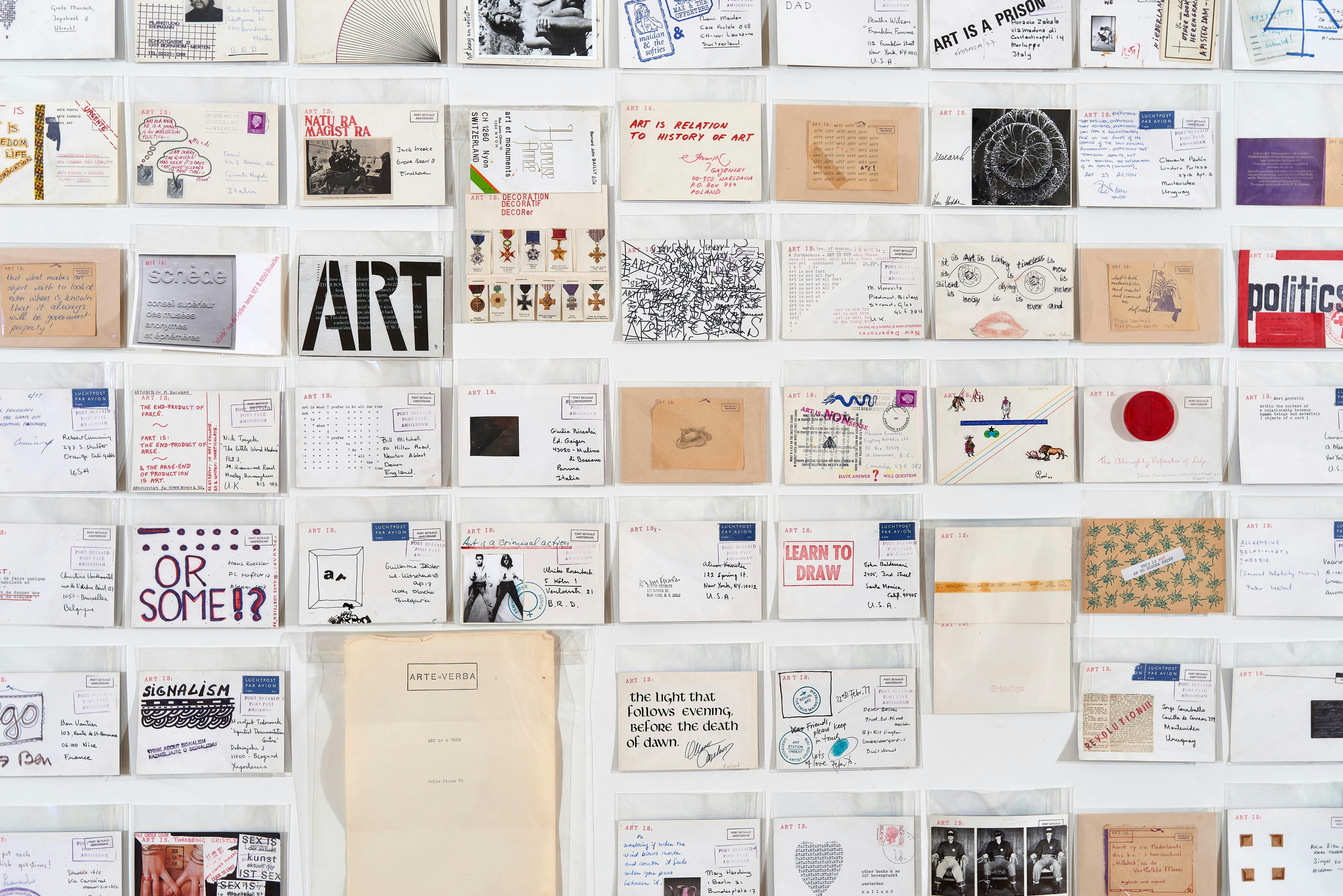 Installation view of Ulises Carrión exhibition showing small collages of varying size, envelopes, photographs, and sketches mounted in a grid to a wall.