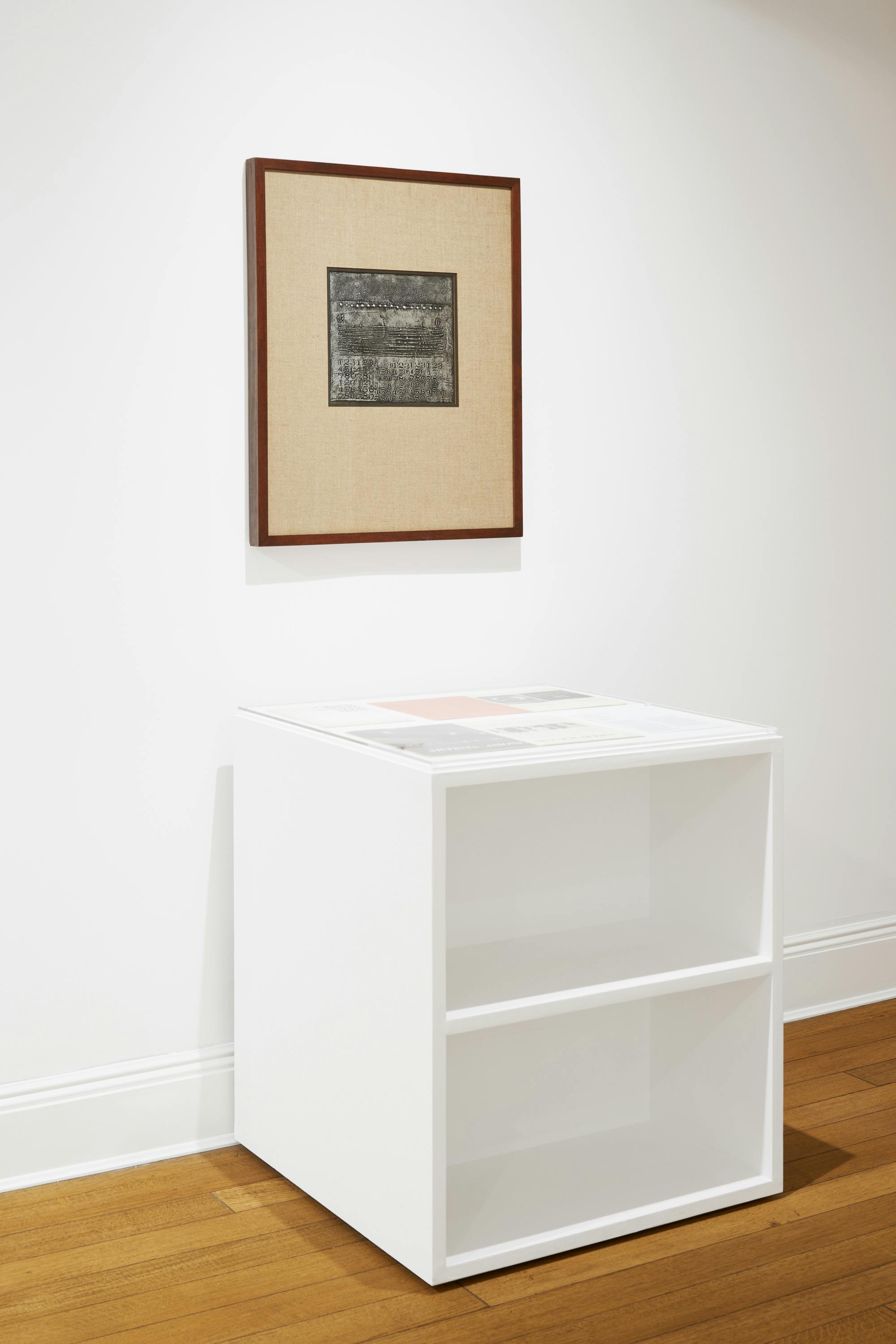 Installation view of a vitrine with a wall-mounted work by José Antonio Fernández-Muro positioned above.