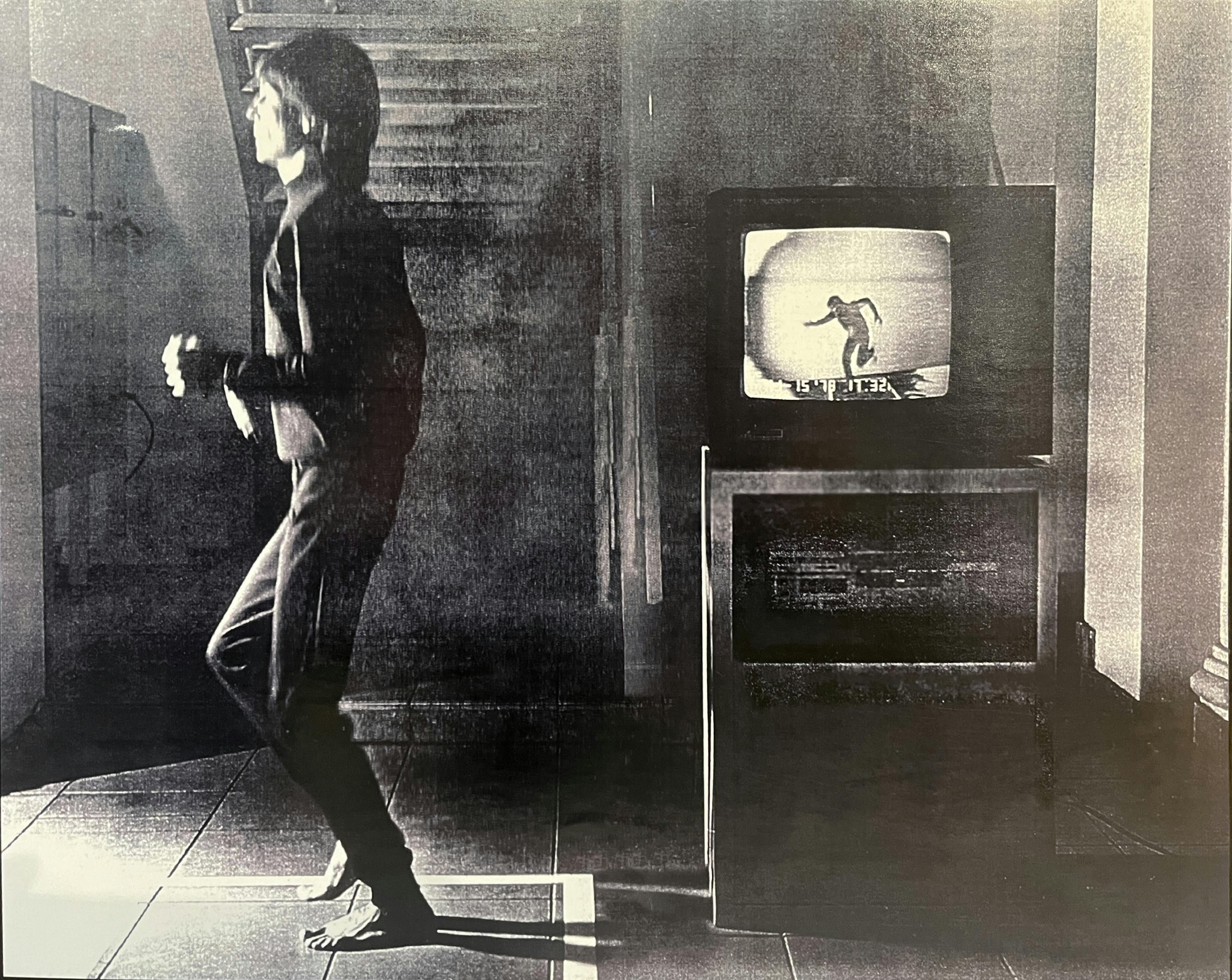 Black-and-white image of person running with a TV monitor in the background showing image of person running