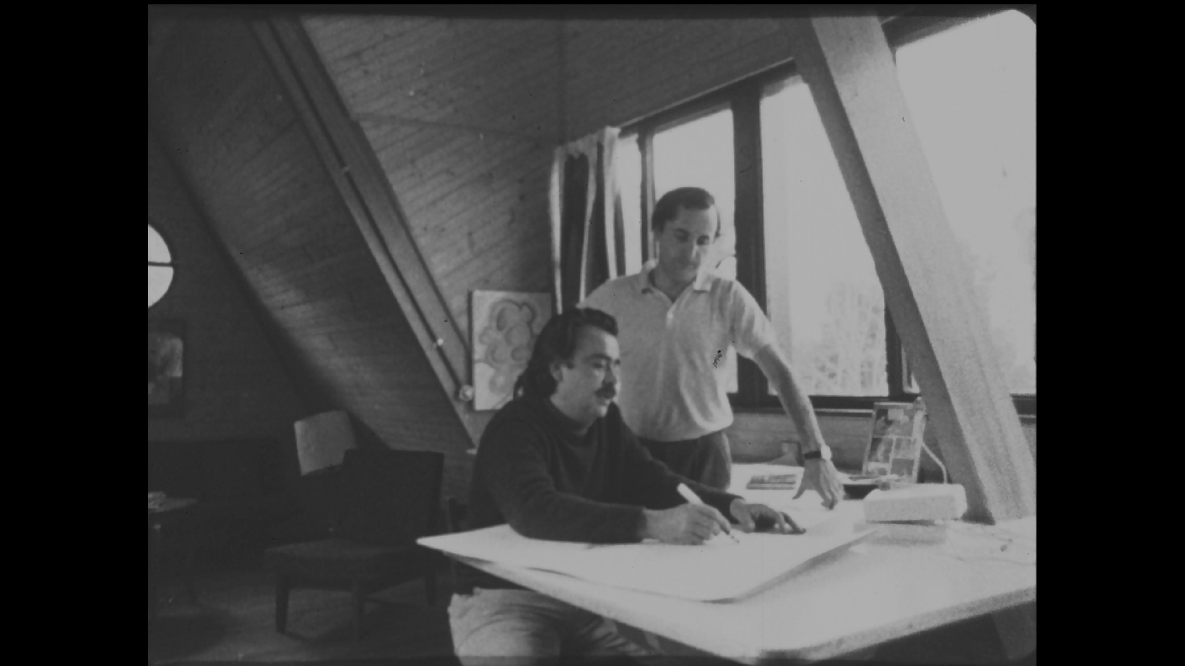 Black-and-white film still of two men working at a desk
