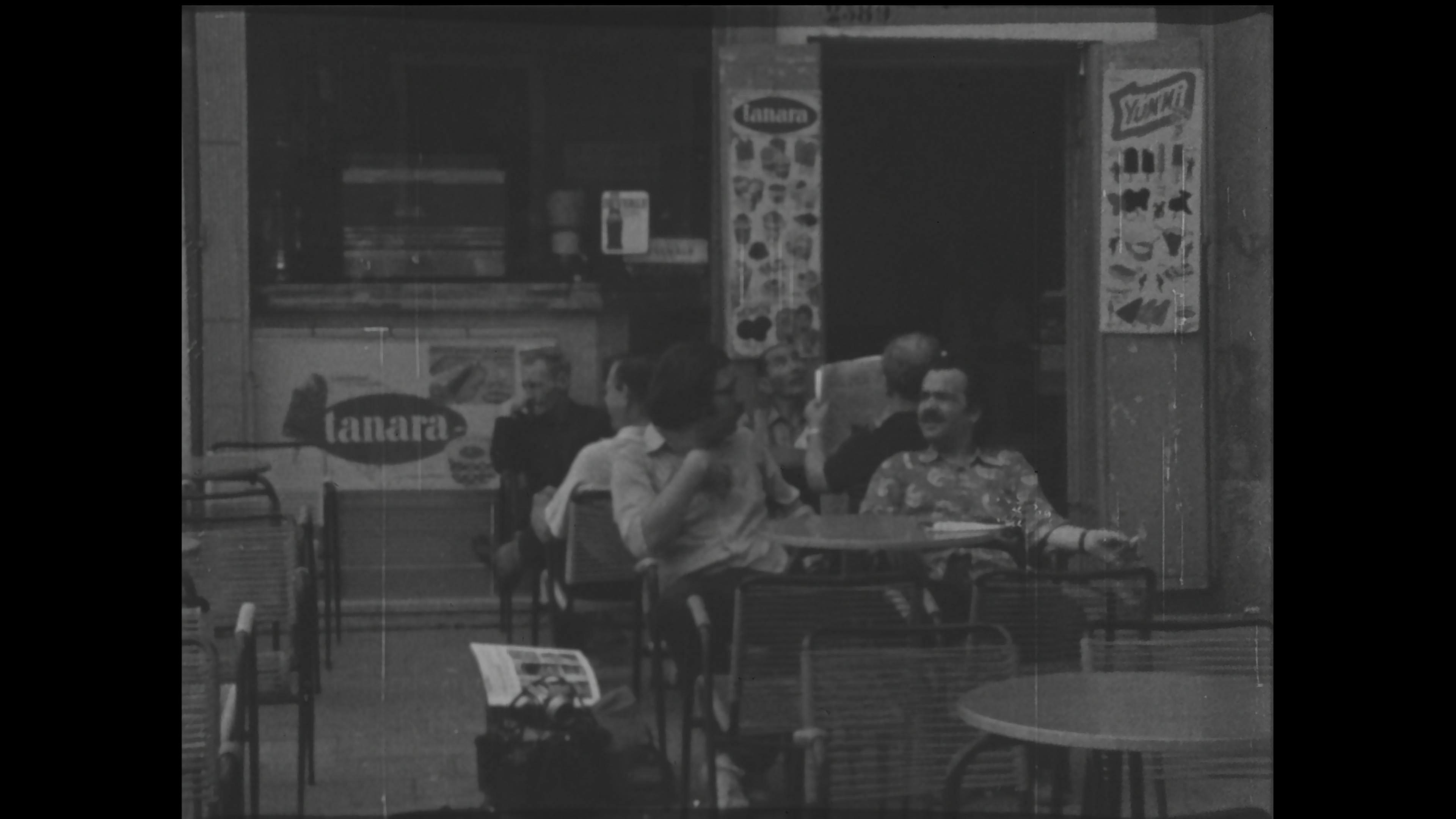 Black-and-white film still of men talking at a café