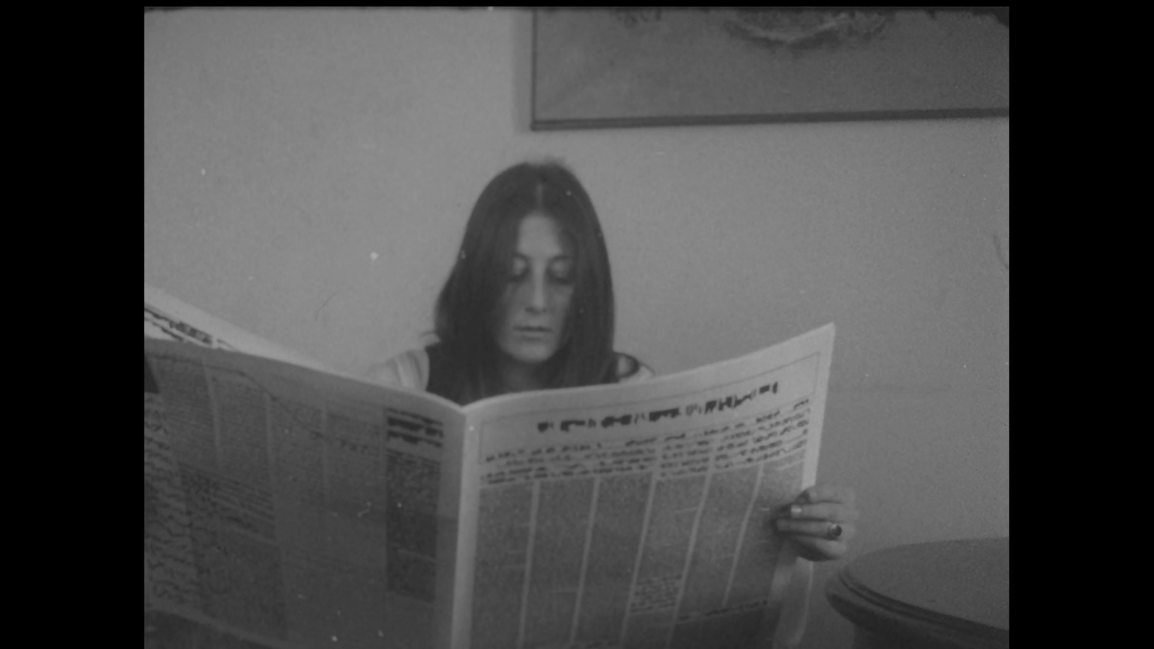 Black-and-white film still of woman reading a newspaper