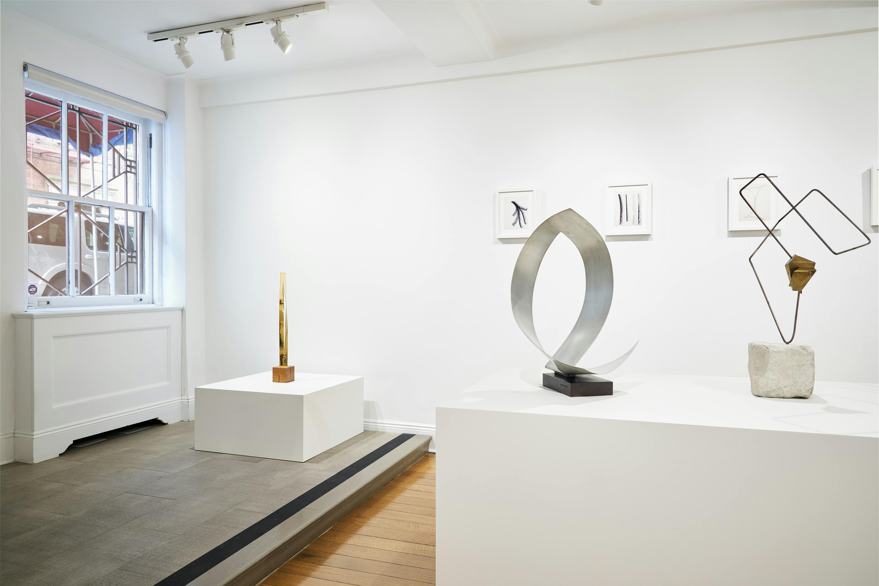 Gallery view of From Surface to Space exhibition showing three free-standing, abstract sculptures and four wall-mounted drawings.