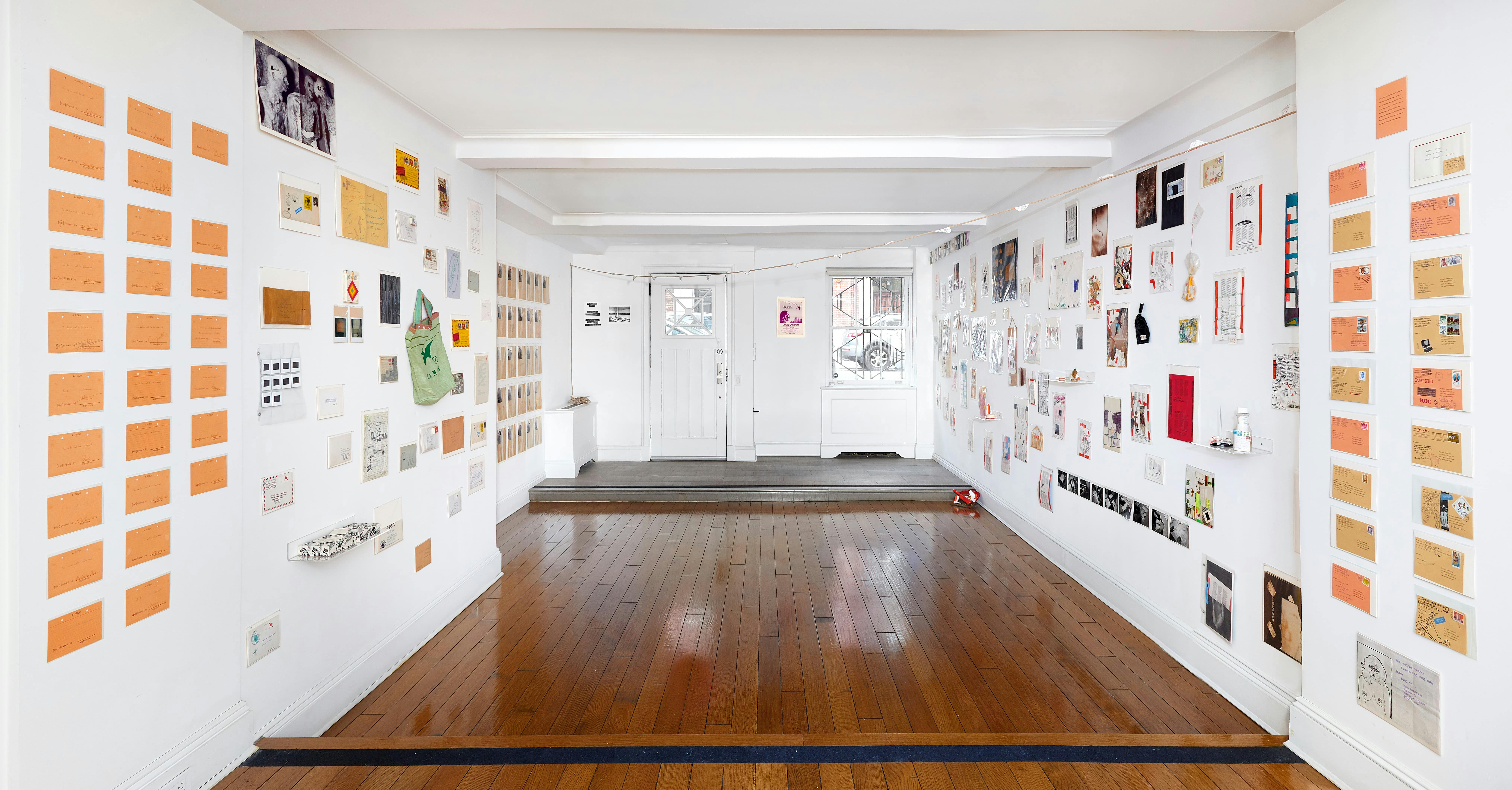Installation view of Ulises Carrión: The Big Monster exhibition showing envelopes, photographs, and various objects mounted to the gallery walls.