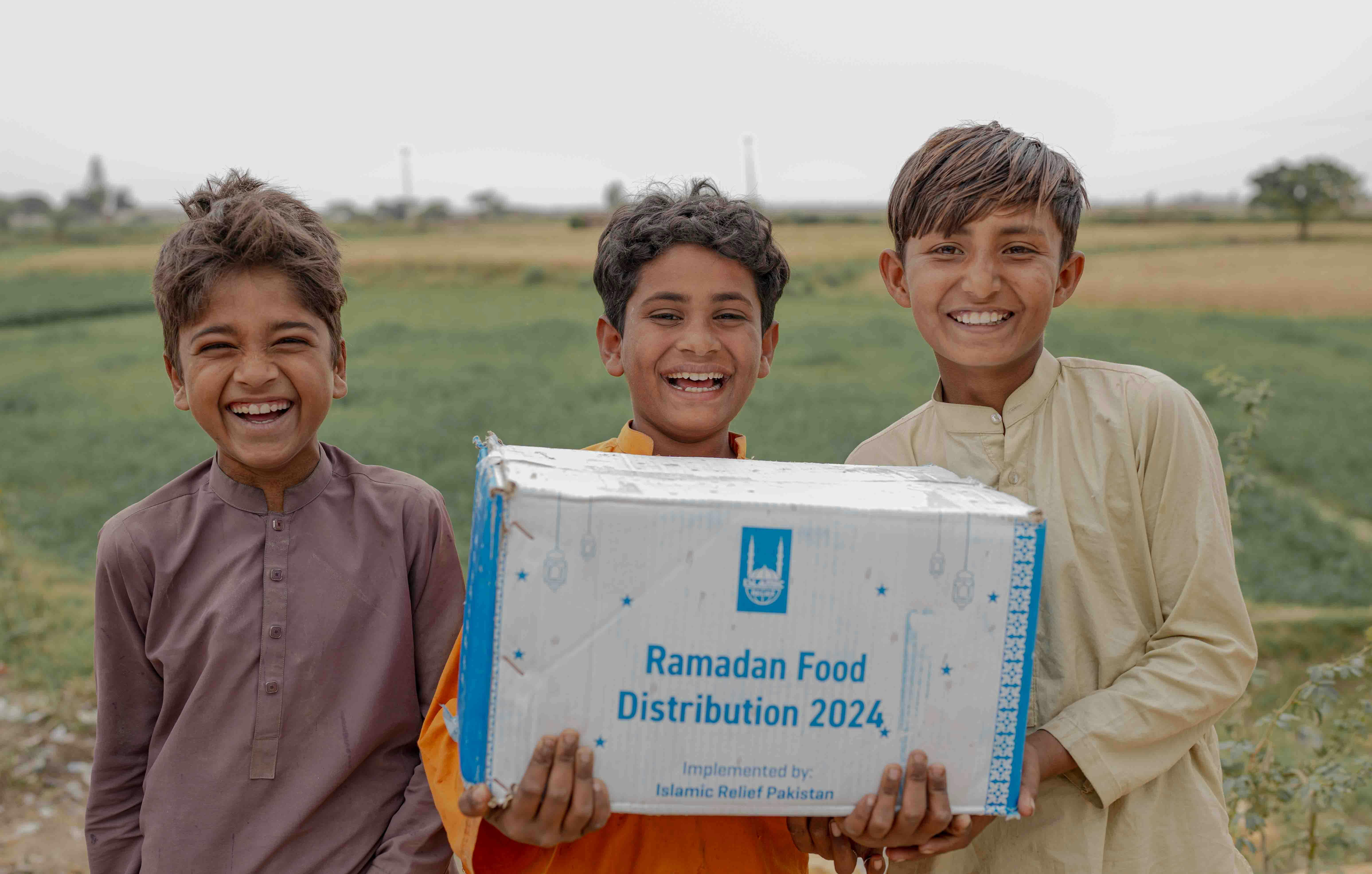 Three smiling children holding an Islamic Relief Ramadan food distribution box