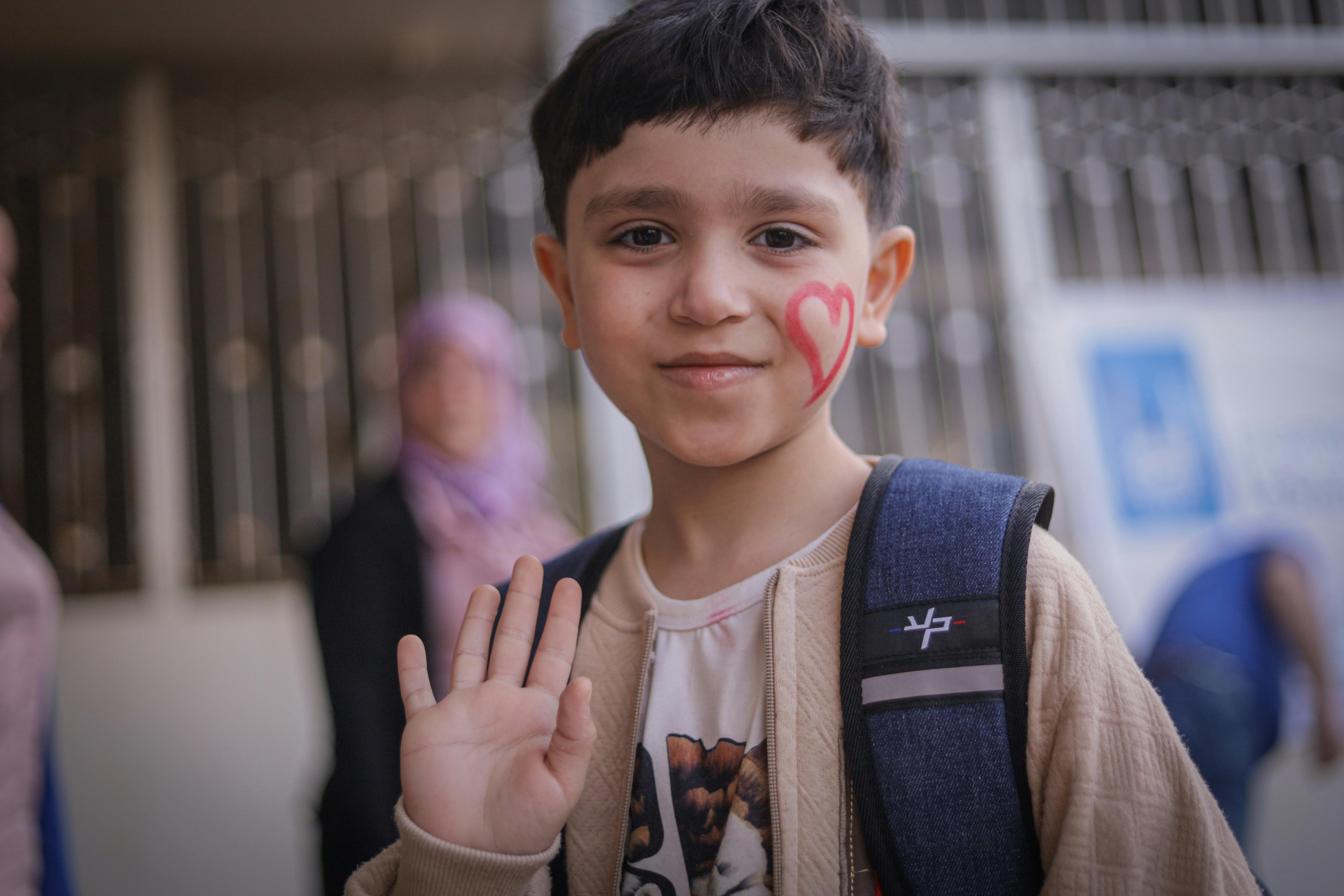 Child waving, with a heart painted onto their cheek