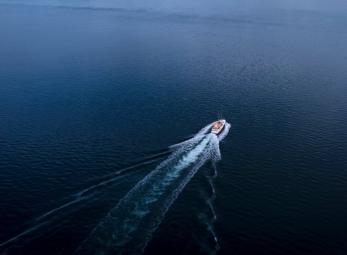 Bátur siglir yfir kyrran sjó og skilur eftir sig spor í vatninu, séð úr lofti.