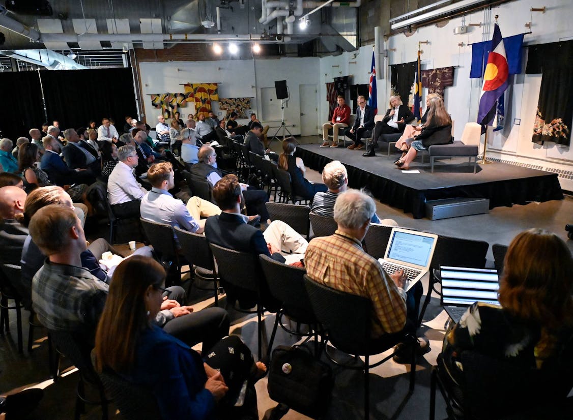 Panel discussion in progress at the 2024 Our Climate Future conference in Colorado, with speakers on stage and a seated audience engaged in the conversation on clean energy and climate solutions. Icelandic and Colorado state flags are visible in the background.