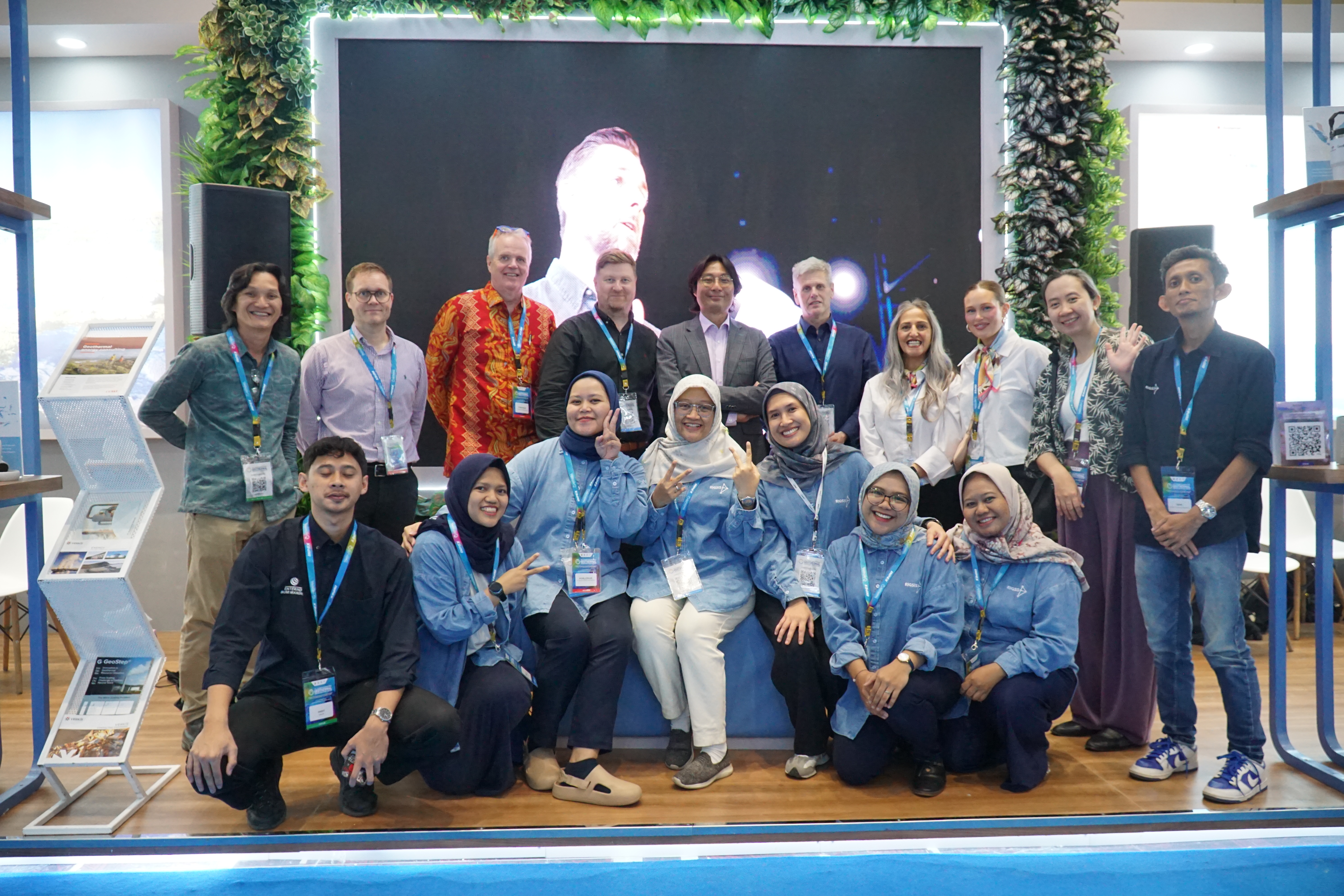  A group of Icelandic business representatives and Indonesian counterparts from Rigsis pose for a photo at the IIGCE 2025 geothermal conference in Jakarta. The individuals stand and kneel in two rows in front of a large screen.