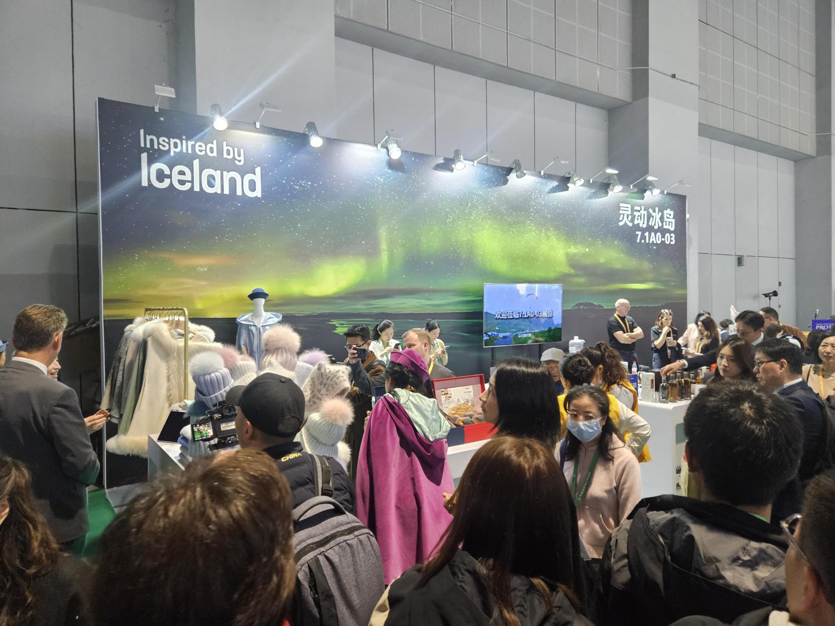A busy, wide view of the "Inspired by Iceland" national pavilion at the China International Import Expo (CIIE). The booth features a large backdrop image of the Northern Lights and is crowded with numerous attendees and a few booth staff members.