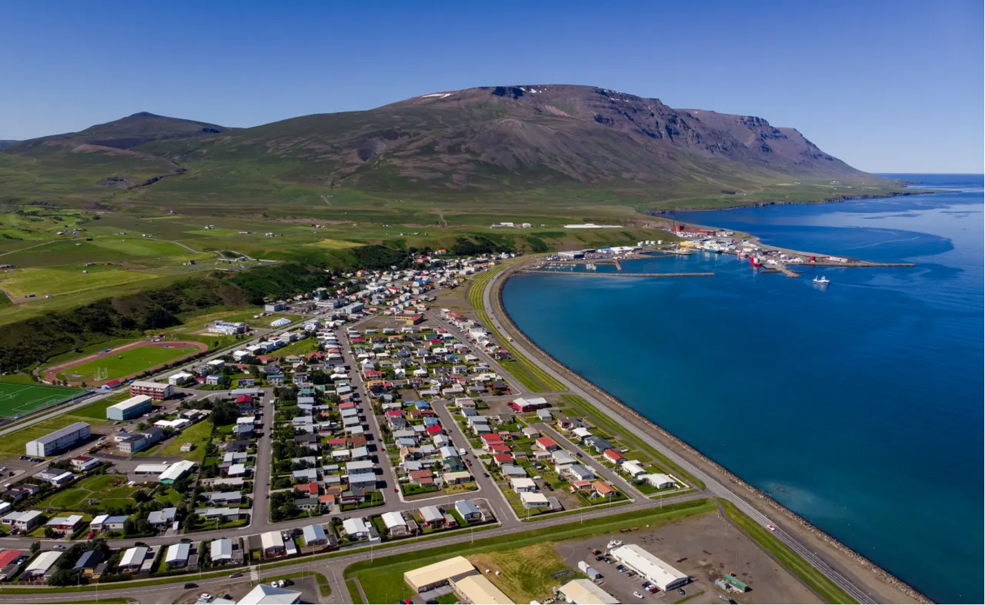 Yfirlitsmynd yfir Sauðárkrók á sólríkum degi, með litrík húsþök og sjórinn í kring  djúpblár að lit