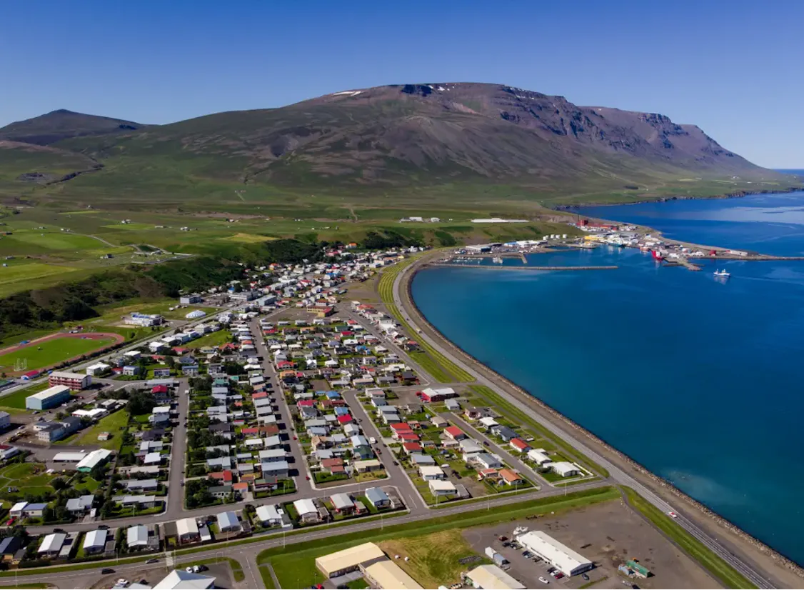Yfirlitsmynd yfir Sauðárkrók á sólríkum degi, með litrík húsþök og sjórinn í kring djúpblár að lit