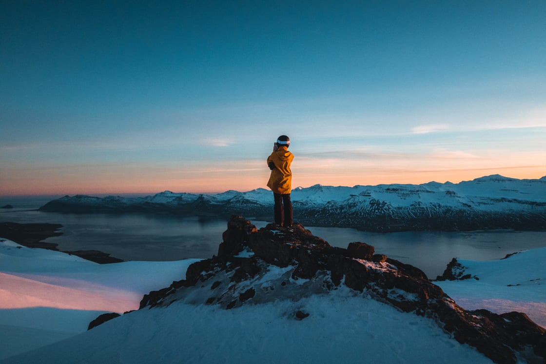 Manneskja á tindi í appelsínugulum jakka á Austfjörðum