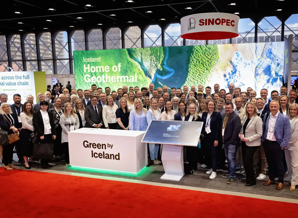 A professional group photograph of the Icelandic delegation at the World Geothermal Congress 2026 in Calgary, featuring representatives from over 20 companies and institutions gathered at the pavilion under the Green by Iceland banner displaying the slogan, Iceland is the home of geothermal.