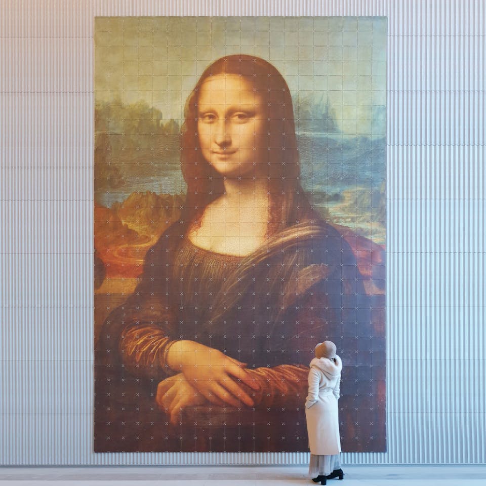 Da Vinci's Mona Lisa groot aan de muur met vrouw met hoed ervoor