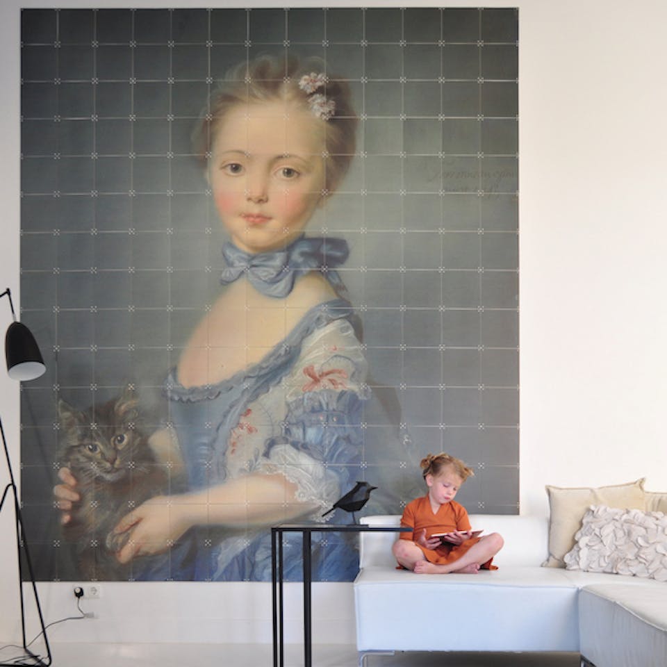 Girl with a kitten van Jean Baptiste Perronneau groot aan de muur boven witte bank met meisje met oranje jurk