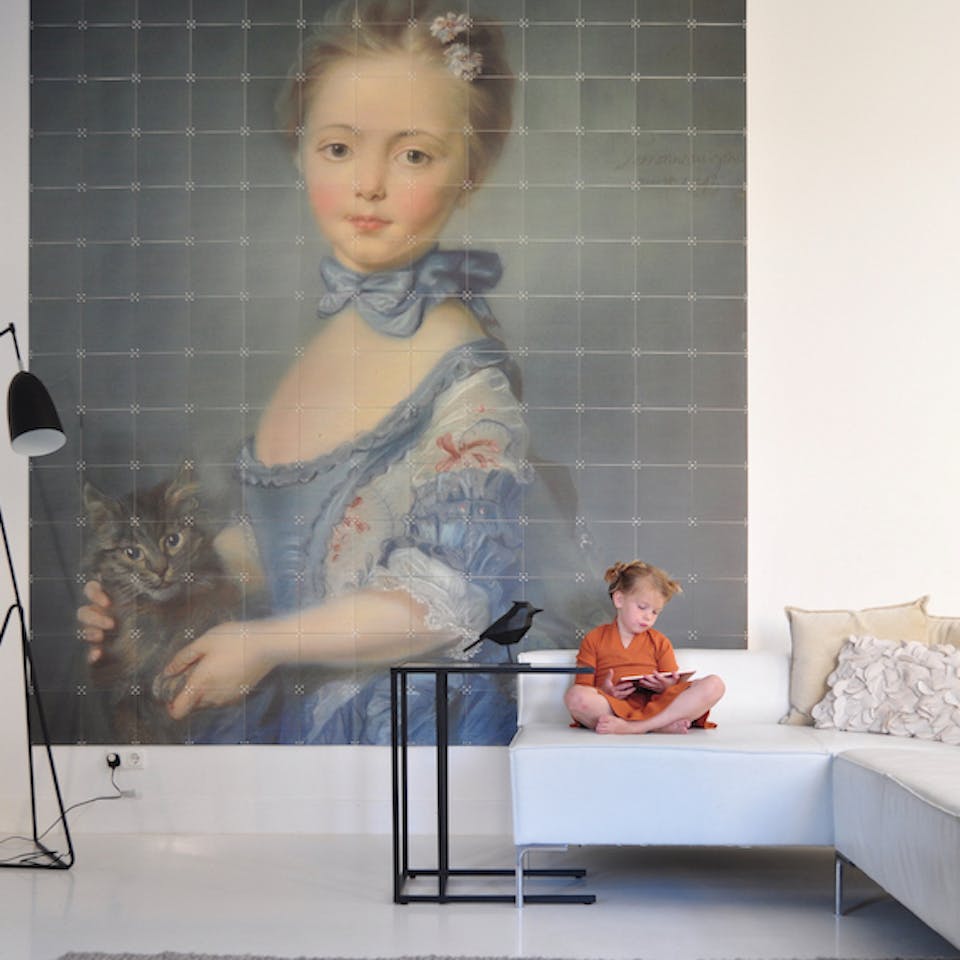 Girl with a kitten van Jean Baptiste Perronneau groot aan de muur boven witte bank met meisje met oranje jurk