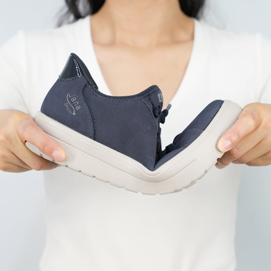 Person drückt einen blauen Jana Step in Sneaker zusammen – das zeigt wie flexibel die Sohle des Sneakers ist.