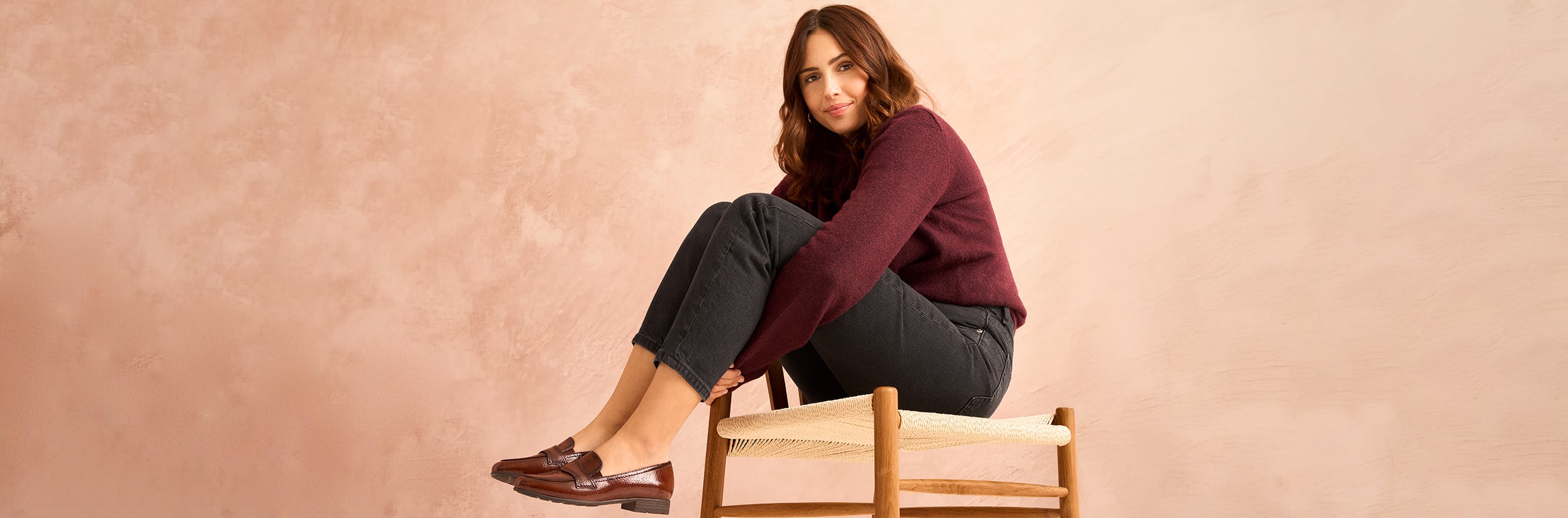 Model sitzt auf einem Holzstuhl und trägt braune Loafer
