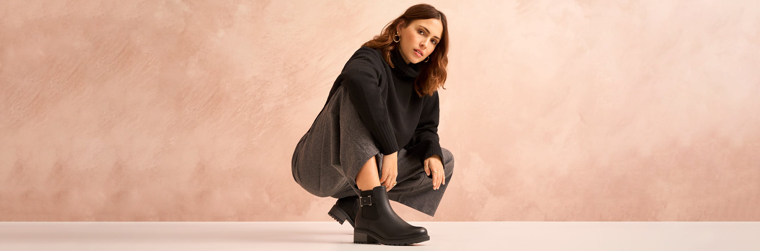 Model hockt und trägt schwarze Stiefeletten mit einer Schnalle an der Seite