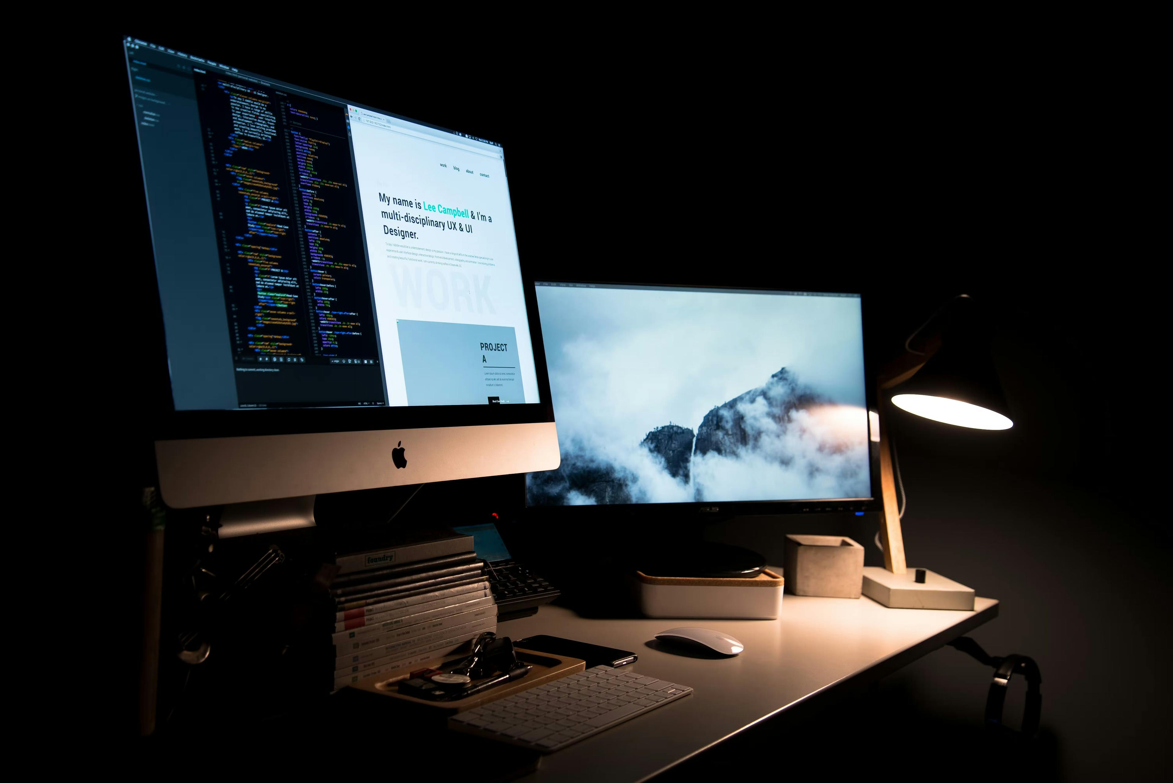 Dual screen apple computer on a desk at night.