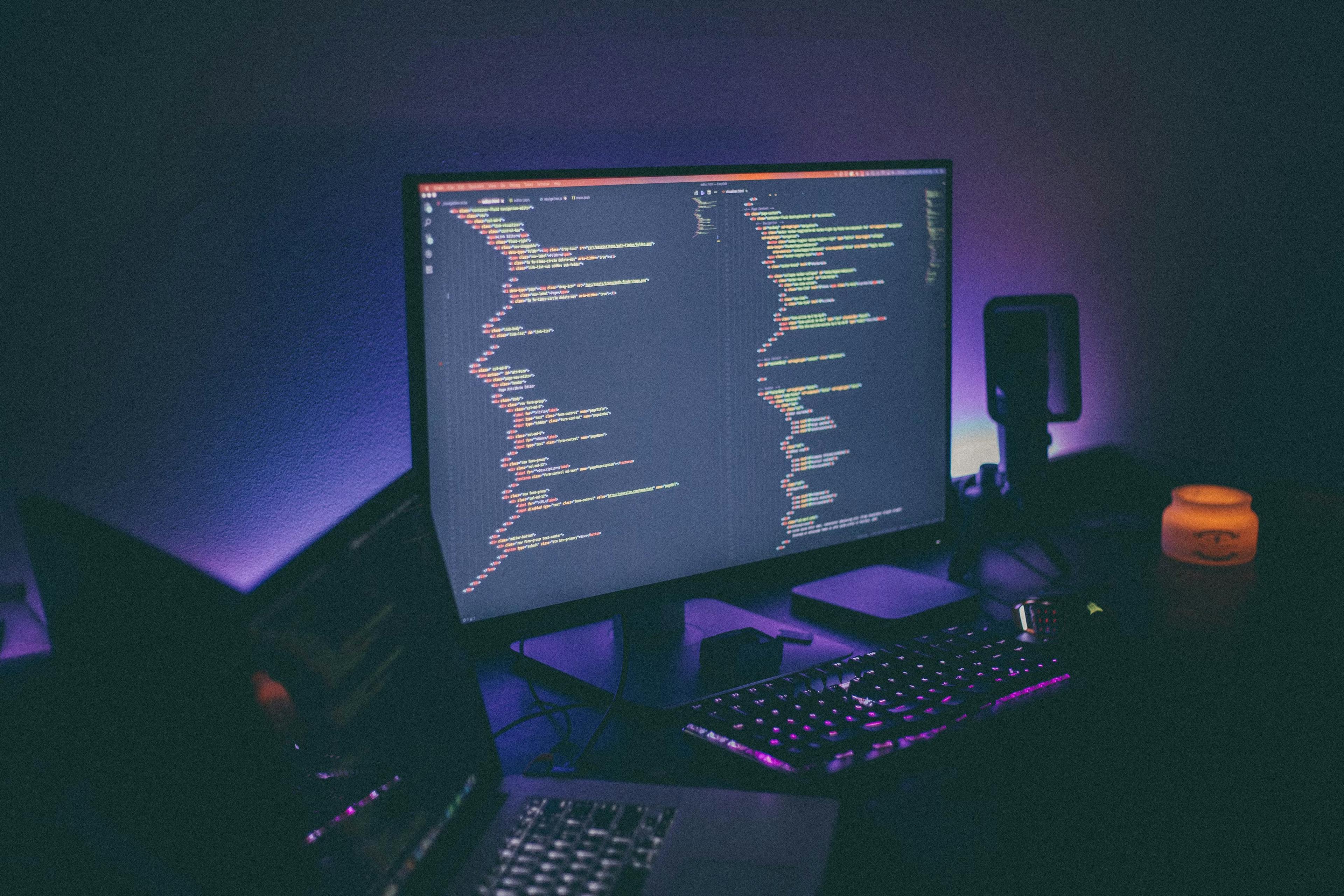 Computer in a dark room featuring code on the screen