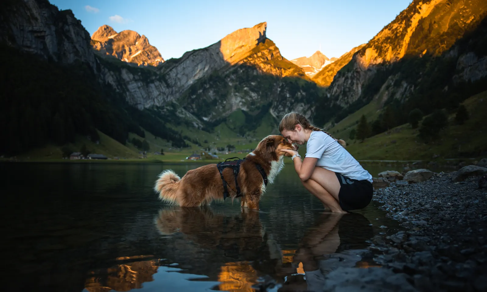 Eine Frau mit Hund in einem See, im Hintergrund sind Berge