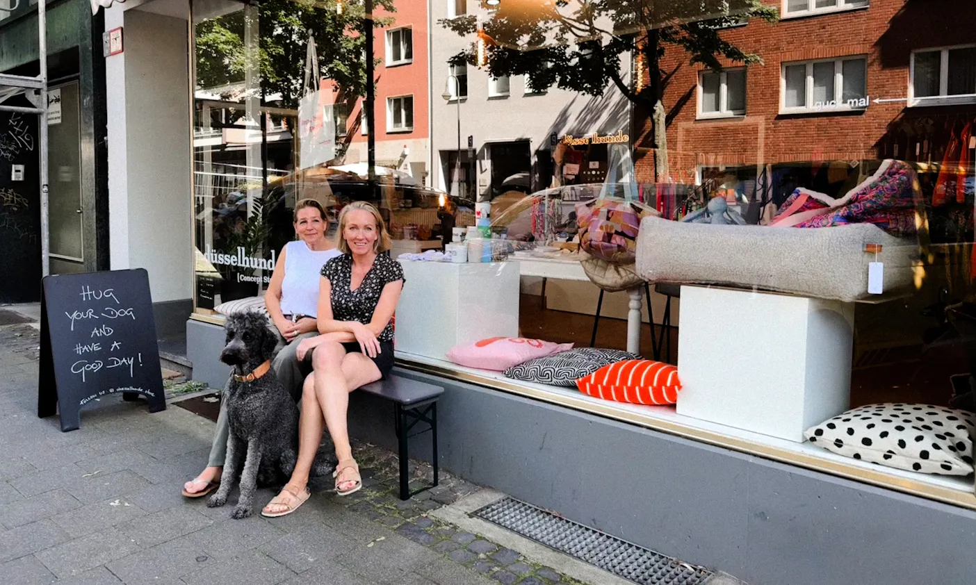 Zwei Frauen mit einem Hund sitzen auf einer Bank vor dem düsselhunde Store in Flingern