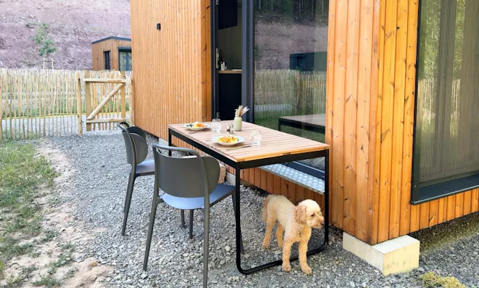 Hund steht unter einem Esstisch im Garten eines DOGGIA Tiny Houses