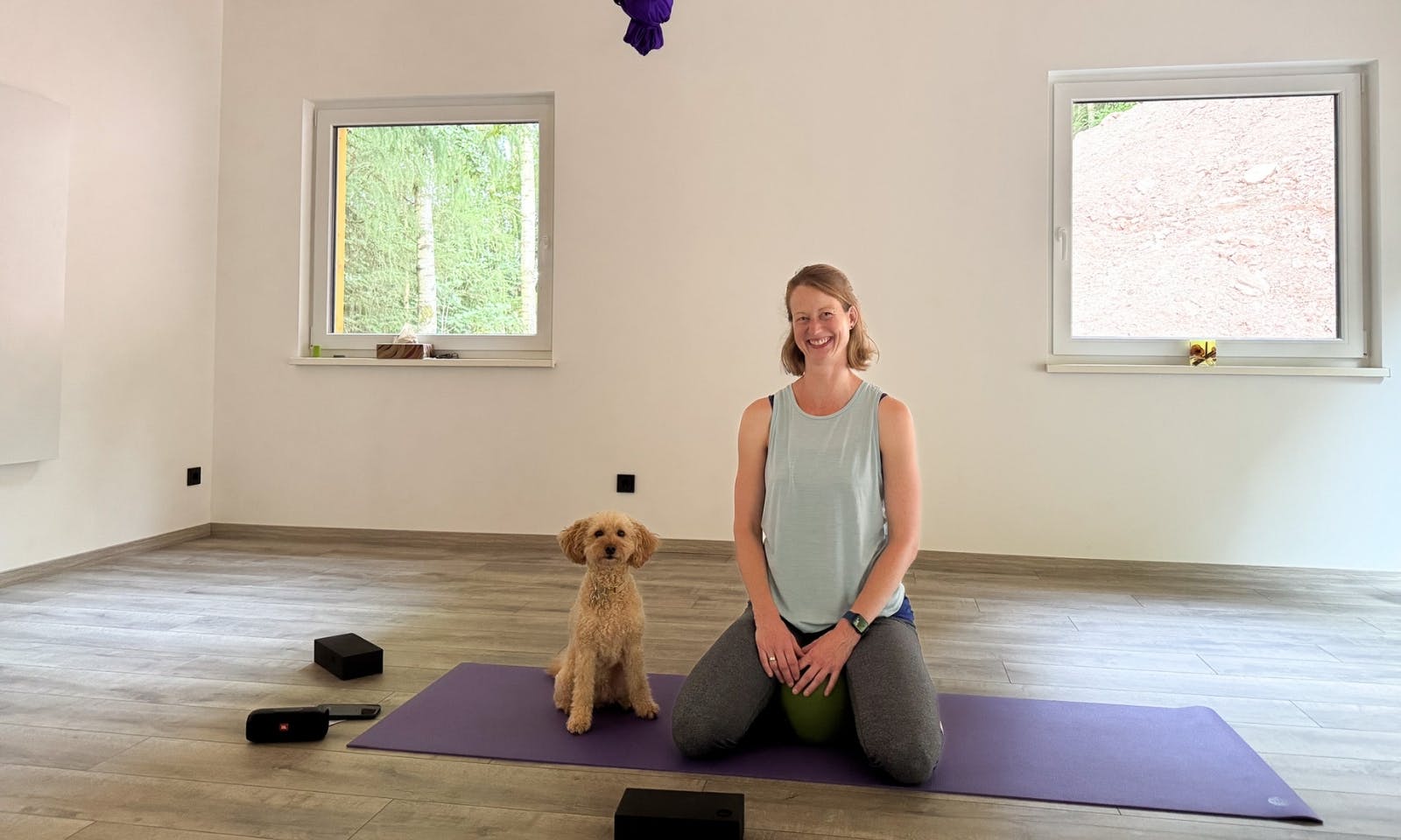 Eine kniende Frau mit einem Hund auf einer Yoga-Matte im DOGGIA