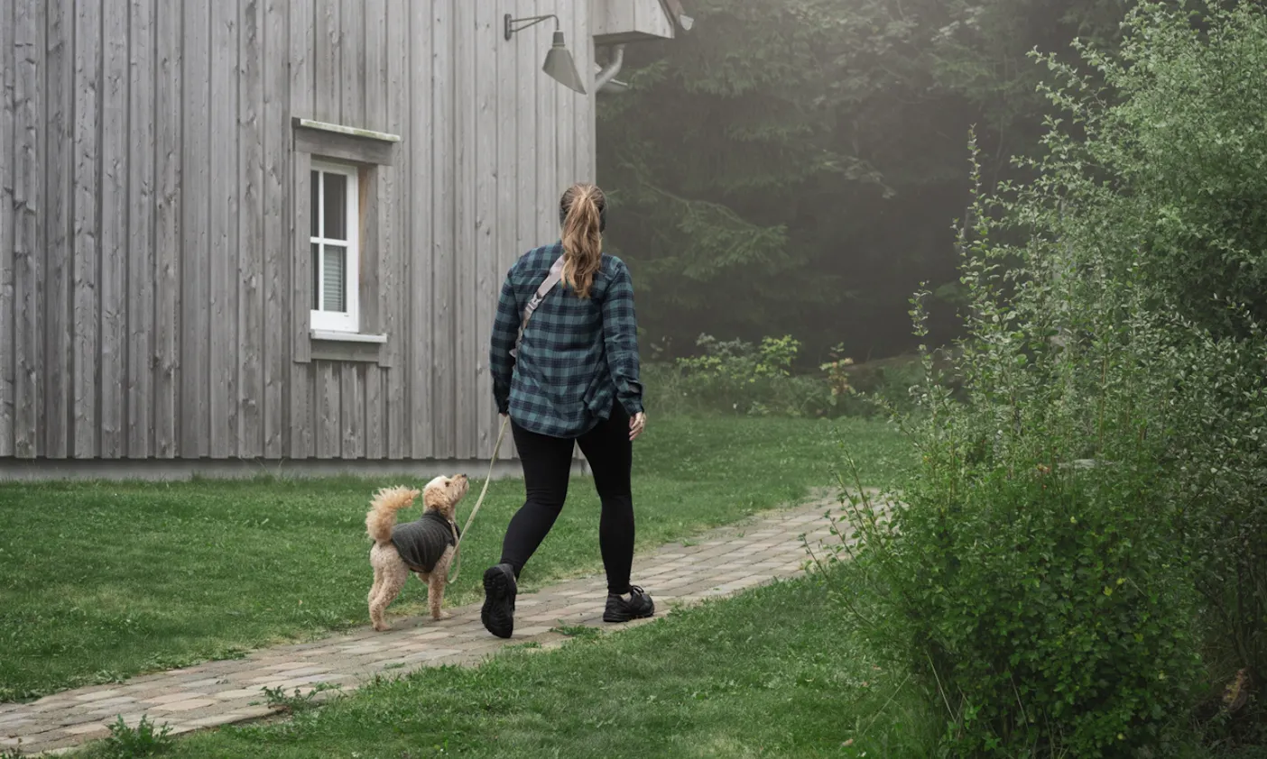 Eine Frau geht mit ihrem Hund in Richtung Ferienhaus im Torfhaus Harzresort