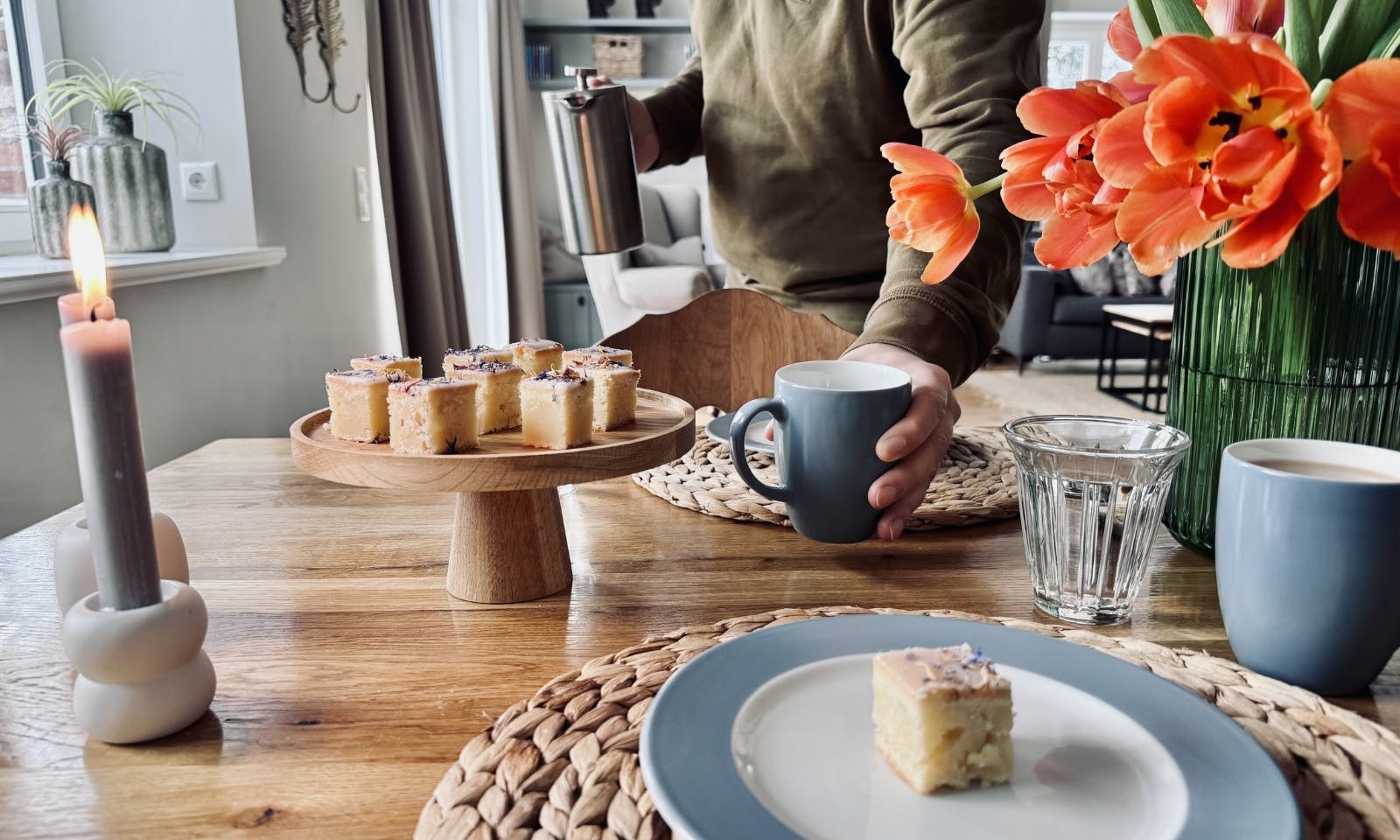 Küchentisch gedeckt mit Kuchen, Tellern, Kerzen, Geschirr und Tulpen