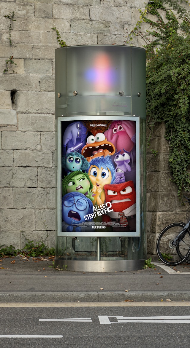 Ein Plakatwerbeträger mit einem bunten Plakat von 'Inside Out 2' an einer Steinmauer.
