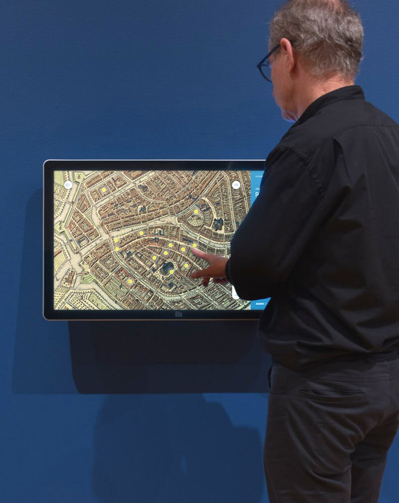 A man interacting with a touchscreen displaying Rembrandt's Leiden in the exhibit Leiden circa 1630: Rembrandt Emerges at the Agnes Etherington Art Centre.