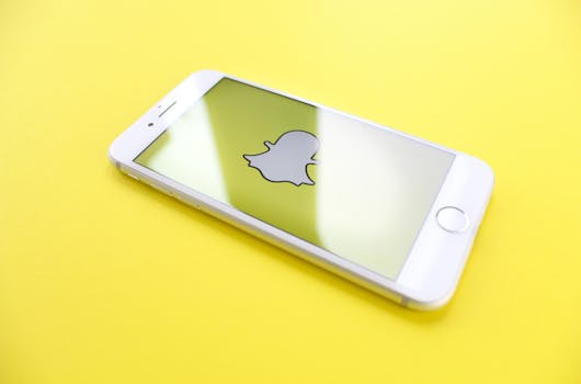 A white iphone with the Snap logo on the screen on a plain yellow background