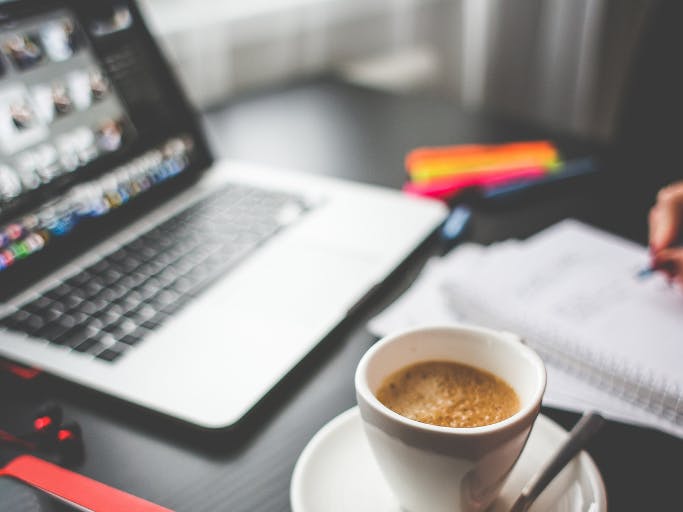laptop next to coffee cup and notebook