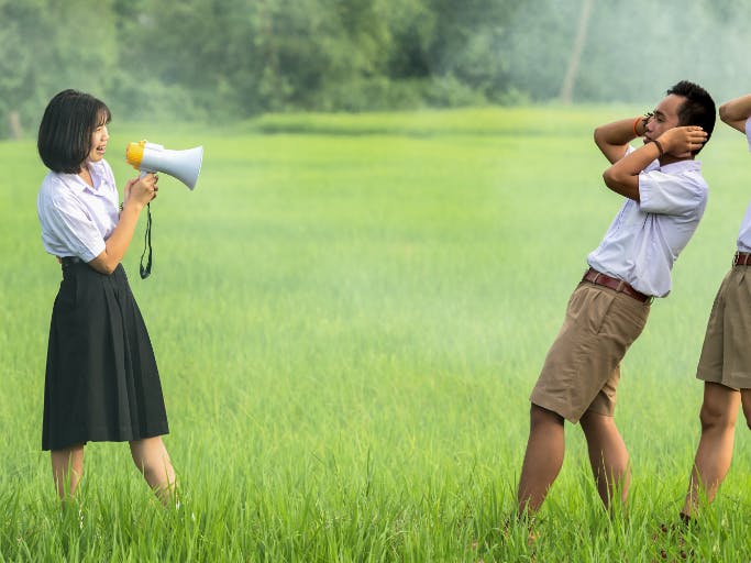 woman with bullhorn and two men covering their ears