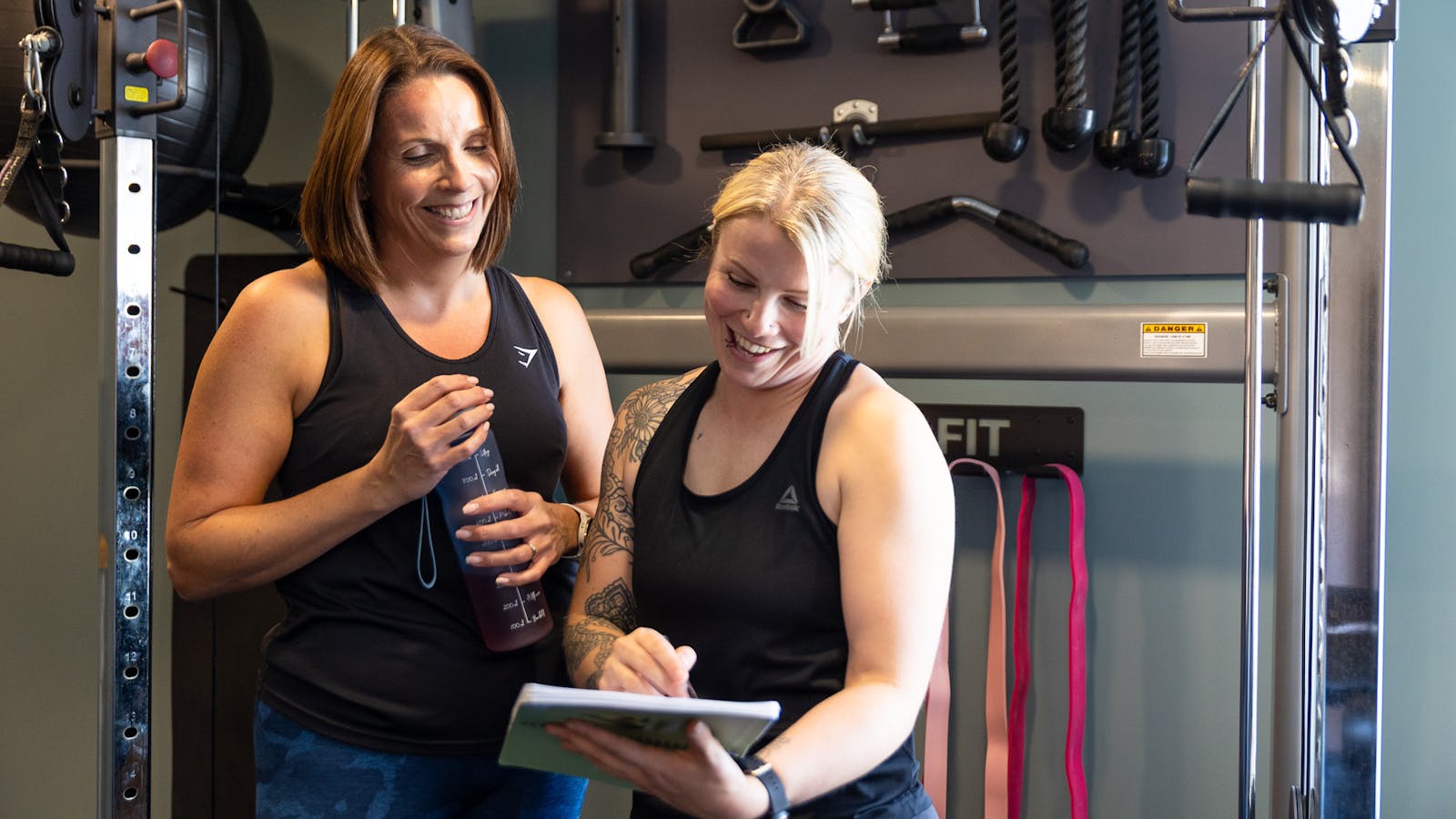 PT talking to a client through weight training book in Jess-fit studio
