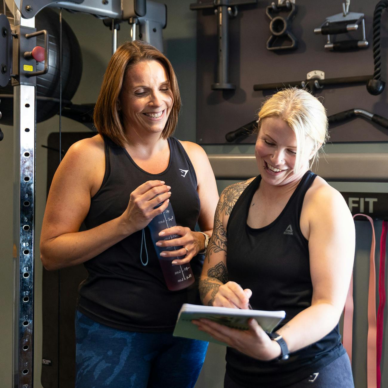 PT talking to a client through weight training book in Jess-fit studio