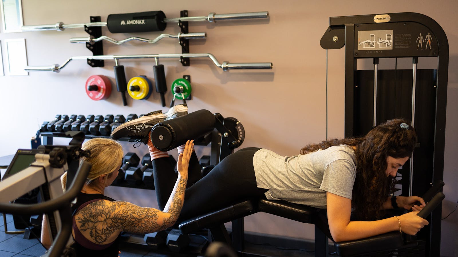 PT talking to a client on prone Leg curl machine in Jess-fit studio