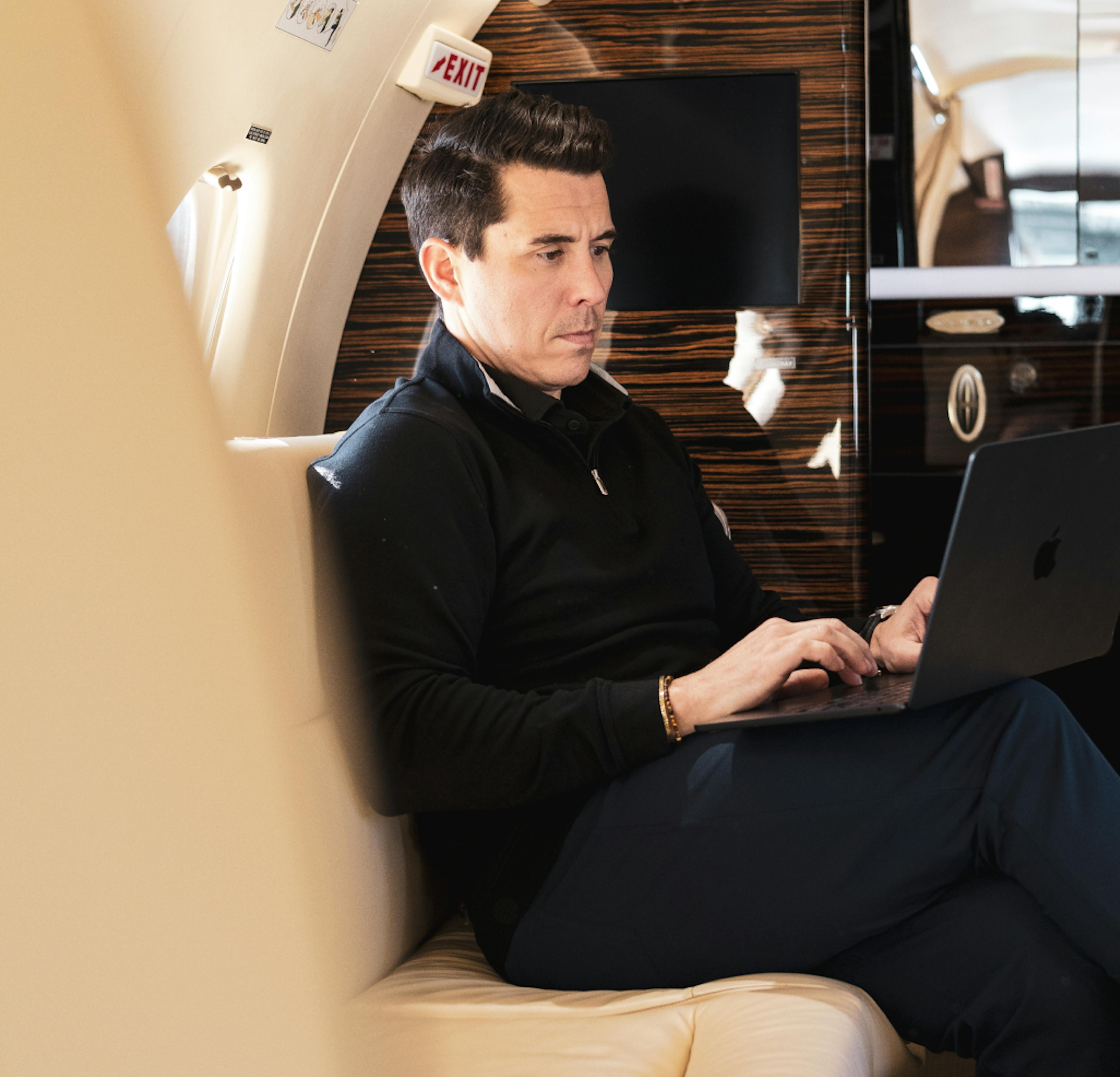 a photo of a man sitting in a private jet working on a laptop