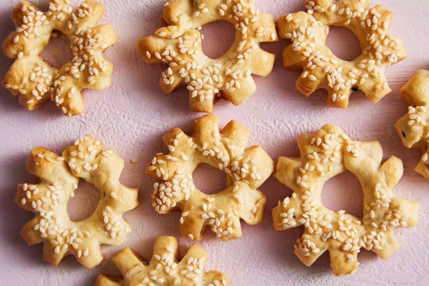Ka'ak sprinkled with sesame seeds atop pink surface.