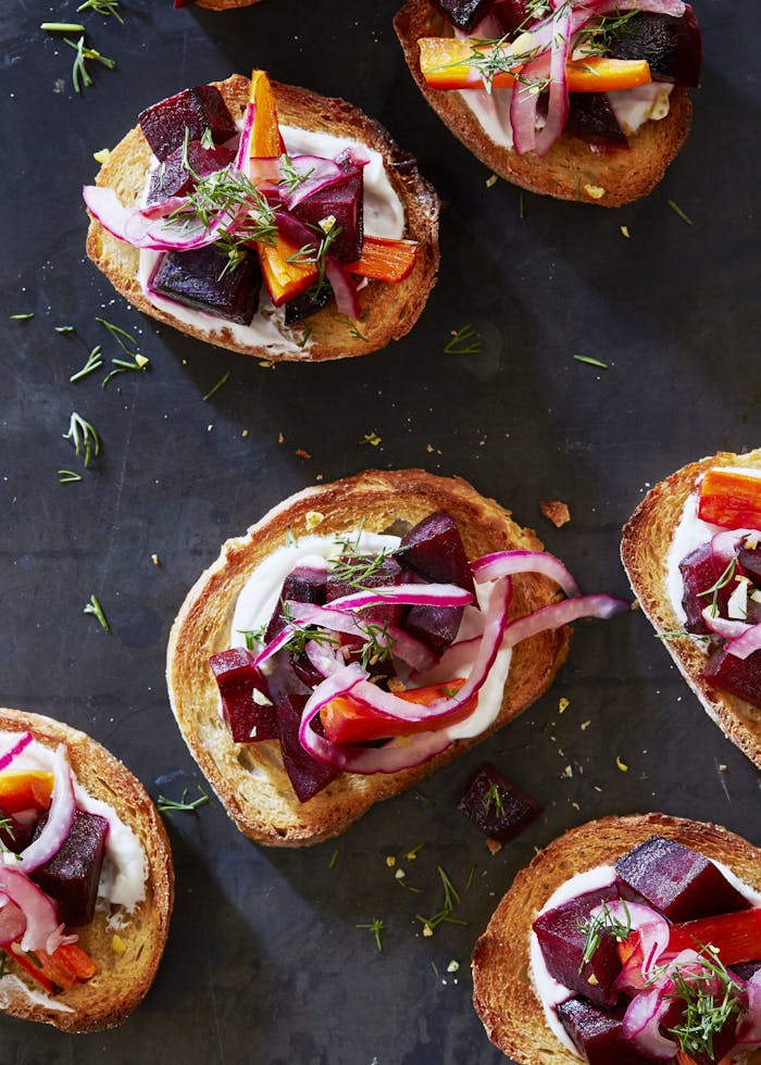Borscht crostinis garnished with dill atop black surface.